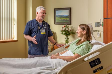 Inpatient Services - Male nurse in scrubs at patient's bedside