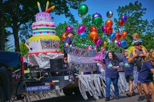 A parade float depicting a giant birthday cake with colorful balloons 