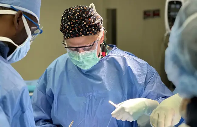 A surgeon in mask and scrubs works on a patient.